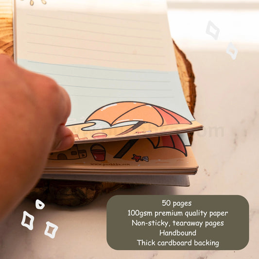 A hand is holding open a cute beacg-themed tearaway notepad stack on a wooden coaster over a white marble surface. A dark gray text box in the bottom right corner lists the product features: 50 pages, 100gsm premium quality paper, non-sticky tearaway pages, handbound, and thick cardboard backing.