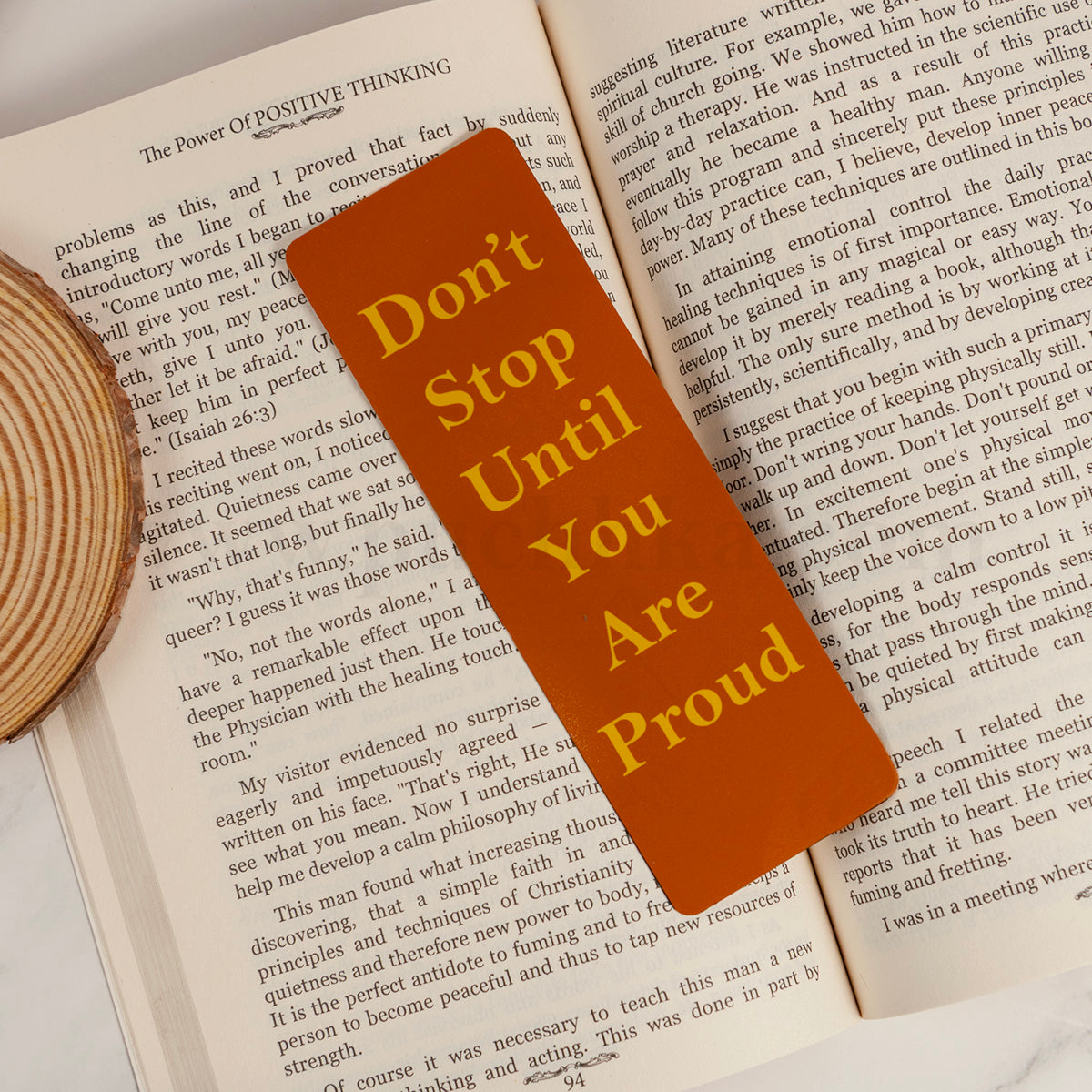 A rectangular orange bookmark with yellow text reading 'Don't Stop Until You Are Proud' placed on open book pages.
