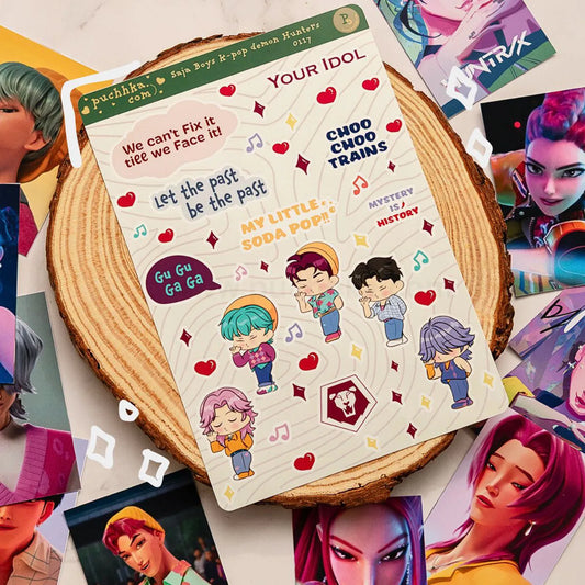 A sheet of cute cartoon character stickers with text like 'Your Idol' and 'Let the past be the past' is displayed on a round wooden slice, surrounded by scattered colorful character cards.