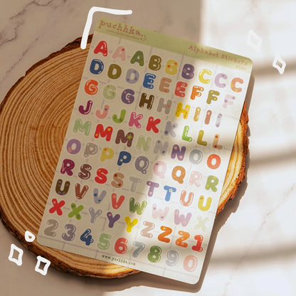 A sheet of colorful alphabet stickers with numbers laminated with glitter matte, displayed on a rustic wood  coaster over a white marble surface with soft shadows.