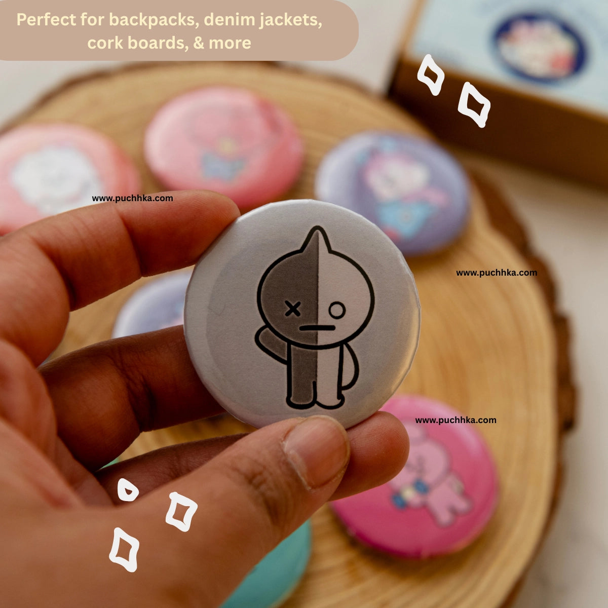 A hand holds a round pinback button featuring a split cartoon character design. The button is shown in front of a wooden tray holding several other colorful round buttons, with a text banner at the top stating 'Perfect for backpacks, denim jackets, cork boards, & more'.