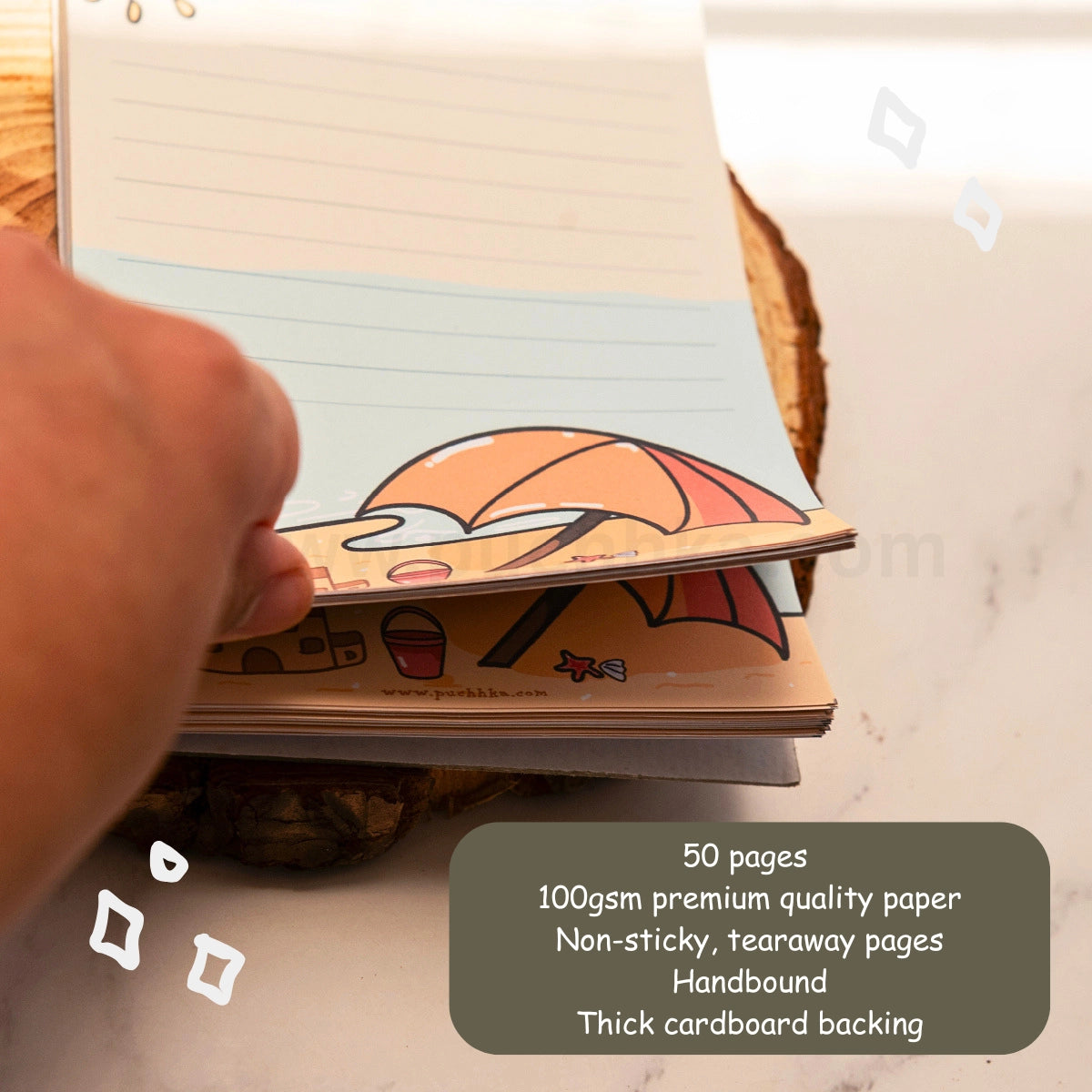 A hand is holding open a cute beacg-themed tearaway notepad stack on a wooden  coaster over a white marble surface. A dark gray text box in the bottom right corner lists the product features: 50 pages, 100gsm premium quality paper, non-sticky tearaway pages, handbound, and thick cardboard backing.