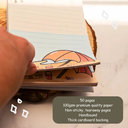 A hand is holding open a cute beacg-themed tearaway notepad stack on a wooden  coaster over a white marble surface. A dark gray text box in the bottom right corner lists the product features: 50 pages, 100gsm premium quality paper, non-sticky tearaway pages, handbound, and thick cardboard backing.