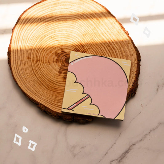 A square tear off memopad with a cute illustration of a pink umbrella on a beach, styled on a rustic wood coaster over a marble surface.