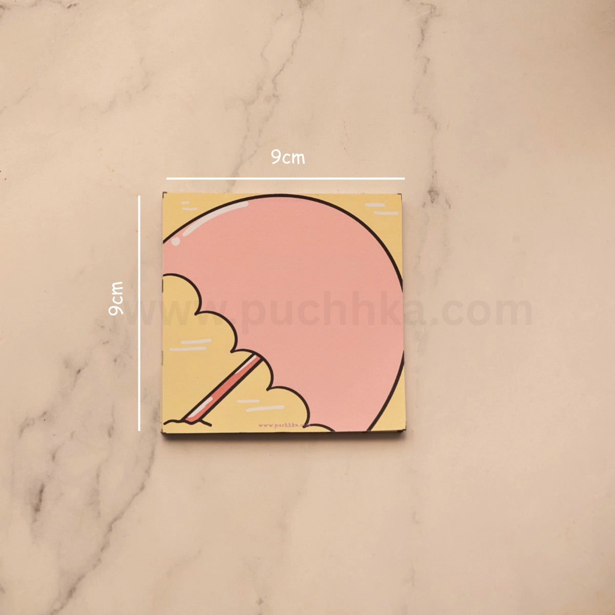 A square coaster with a cute illustration of a pink umbrella on a beach, shown on a light marble surface with 9cm dimension lines indicating its size.