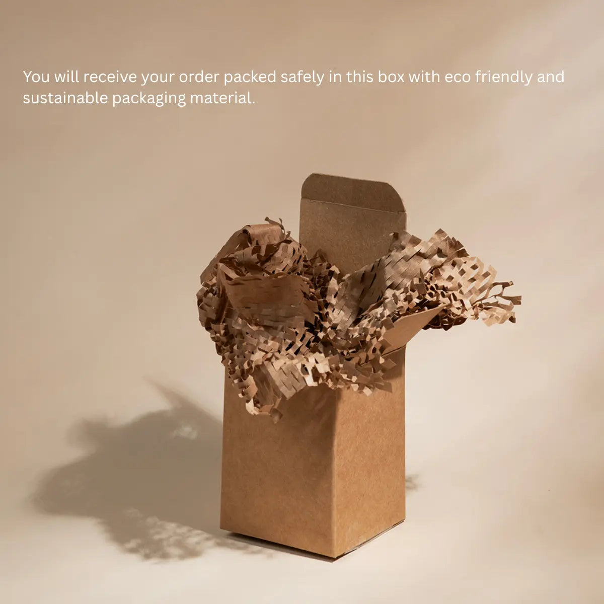 A brown kraft paper box with crumpled brown paper shred packaging, shown on a warm beige background with a text overlay explaining eco-friendly packaging.