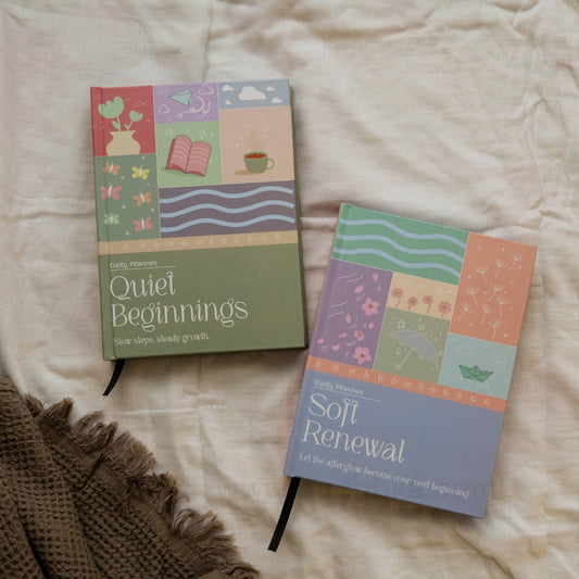 Two illustrated daily planners, 'Quiet Beginnings' and 'Soft Renewal', displayed on a textured cream fabric background with a brown knit blanket corner.