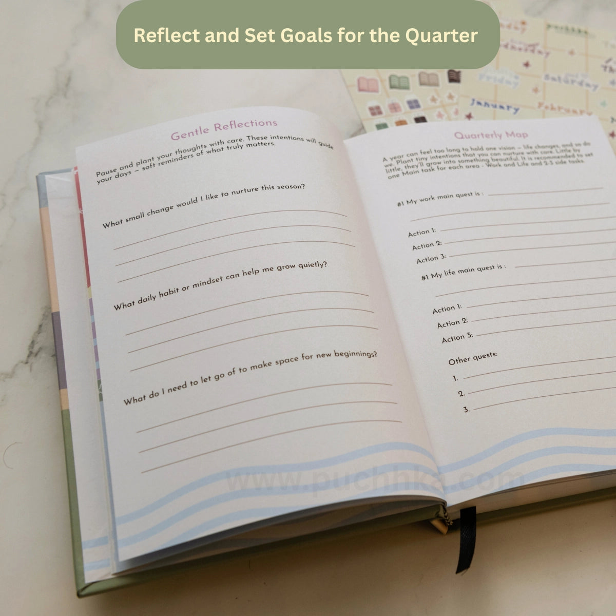An open quarterly reflection and goal-setting journal spread on a light marble surface, with a green banner at the top reading 'Reflect and Set Goals for the Quarter.' The pages show prompts for gentle reflections and a quarterly map with lined writing areas.