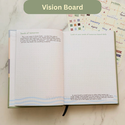 An open Vision Board page in the Daily Planner on a light marble surface, showing dotted pages with inspirational prompts like 'Seeds of tomorrow' and 'Look at your seeds of tomorrow board daily.' A green banner at the top reads 'Vision Board'.