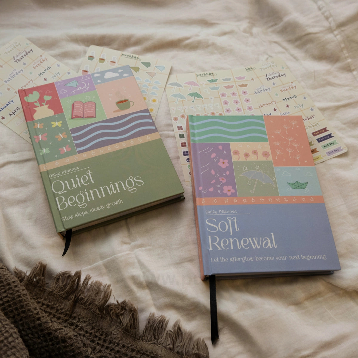 Two illustrated planners lying on a cream fabric surface, with sticker sheets behind them and a fringed knit textile at the lower left. The visible titles are 'Quiet Beginnings' and 'Soft Renewal'; no person or real environment beyond the styled surface is present, so this fits Product/Packaging rather than Lifestyle.