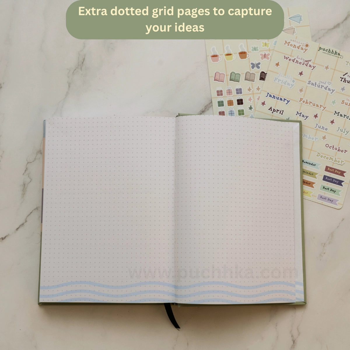 An open planner with dotted grid pages and light blue wavy line accents at the bottom, styled on a white marble surface with sticker sheets behind it and a green text bubble at the top.