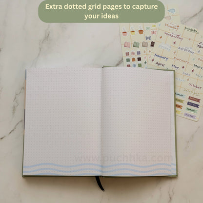 An open planner with dotted grid pages and light blue wavy line accents at the bottom, styled on a white marble surface with sticker sheets behind it and a green text bubble at the top.