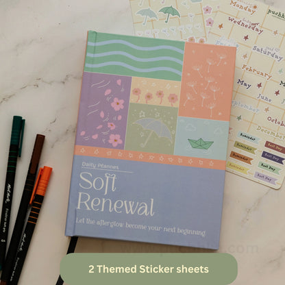 A pastel patchwork hardcover planner titled 'Soft Renewal' lies on a light marble surface with decorative sticker sheets and three pens nearby. The cover shows colored panels with floral, striped, umbrella, and paper boat illustrations.