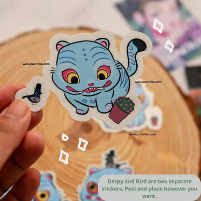 A hand holds a die-cut sticker featuring a cute blue cartoon bird character with a small potted cactus, with other stickers and a wooden slice background visible.