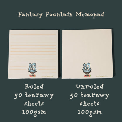 Two cream-colored memo pads labeled 'Fantasy Fountain Memopad' on a dark green background. The left pad is ruled and the right pad is unruled, both with a small fountain printed near the bottom.