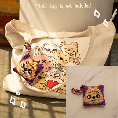 A cream canvas tote bag with a printed skzoo illustration on the front, shown alongside a small Purple and Brown cross-stitch style skzoo bag hanging with a matching strap. The image includes text stating '*Tote bag is not included' and a small inset showing the pouch alone on a marble surface.