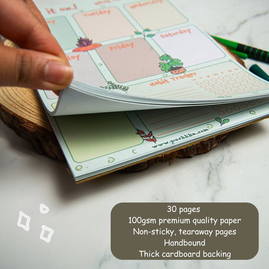 A hand is lifting a page from a tearaway planner notepad with weekly planner pages visible. The notepad has a thick cardboard backing and a dark brown text overlay at the bottom right detailing its specifications.