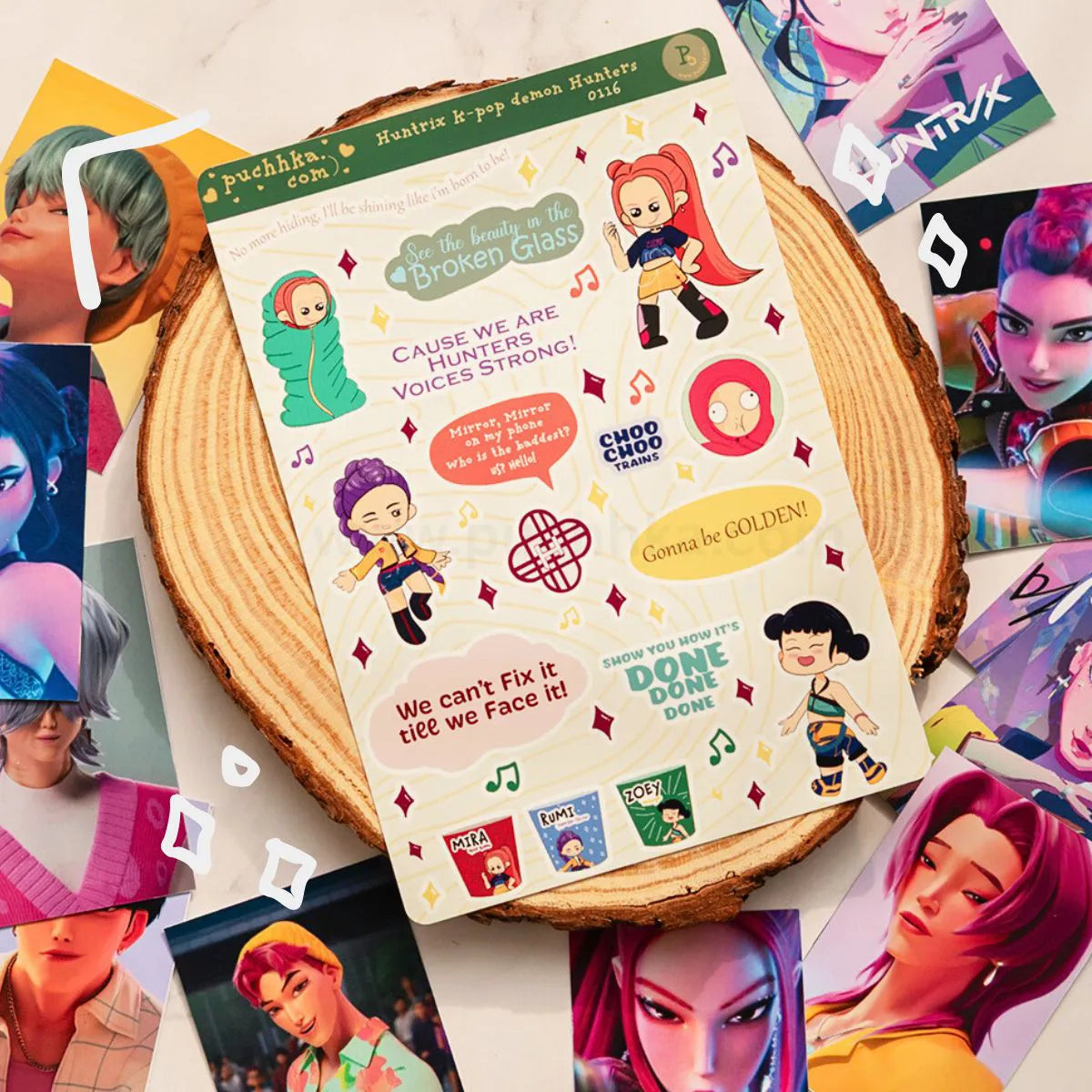 A sheet of colorful character stickers displayed on a round wood slice, surrounded by scattered character art cards. The sticker sheet features illustrated anime-style characters with motivational quotes and music note graphics.