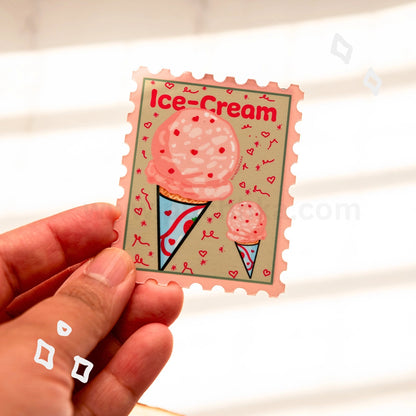 A hand holds a postage-stamp-style sticker featuring pink ice cream scoops in cones on a beige background with the words “Ice-Cream” at the top.
