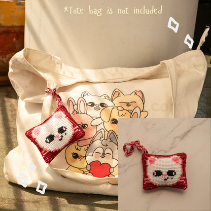 A cream canvas tote bag with a printed skzoo illustration on the front, shown alongside a small red and white cross-stitch style skzoo bag hanging with a matching strap. The image includes text stating '*Tote bag is not included' and a small inset showing the pouch alone on a marble surface.