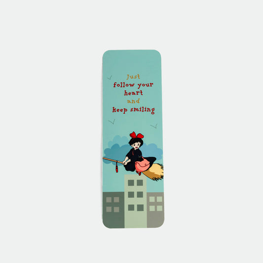 A vertical rectangular bookmark with rounded corners, featuring a light blue-green background with the text 'Just follow your heart and keep smiling' in red and yellow, plus an illustration of a witch riding a broomstick above stylized buildings.