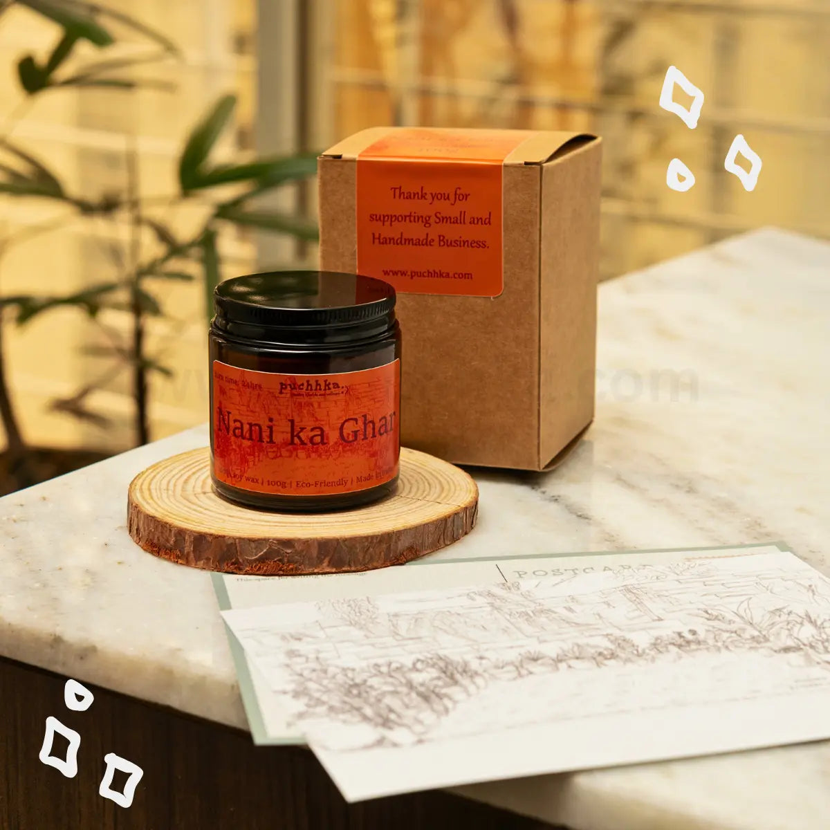 Nani ka ghar scented candle on a wooden slice coaster next to its kraft paper packaging box, set on a marble countertop with a sketch card in front.