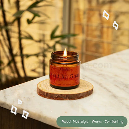 A lit amber glass jar candle labeled 'Nani ka Ghar' sits on a round wood slice coaster on a white marble surface, with a warm blurred indoor background and decorative doodle overlays.