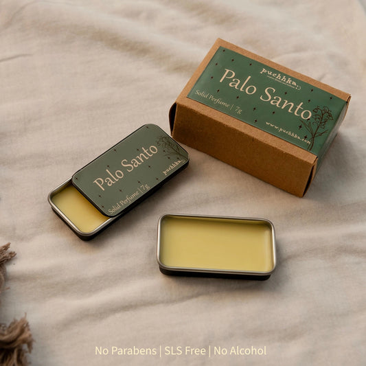 A small rectangular metal tin of Palo Santo wax shown open beside its kraft paper box and a second closed tin, all labeled Palo Santo, on a beige fabric surface.