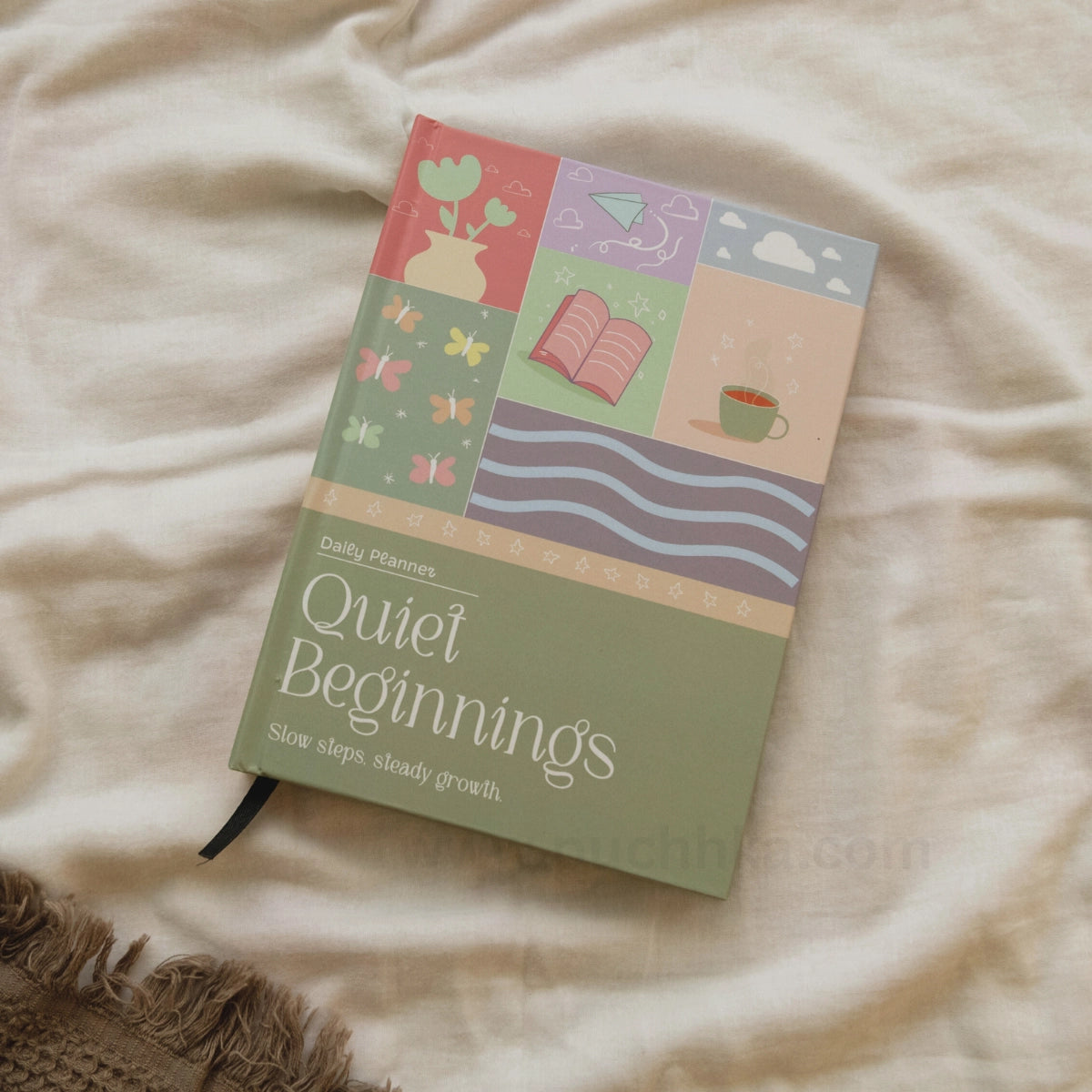 A Daily planner  'Quiet Beginnings' planner by Puchhka, featuring a pastel multicolor cover illustration, resting on a beige fabric background.