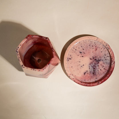 A pink marbled hexagonal tumbler shown next to its matching round lid on a light beige background.
