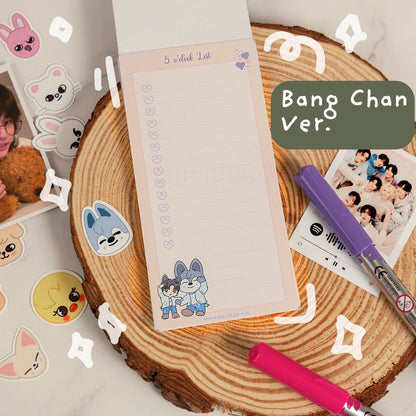 A cute  notepad featuring cartoon characters and the text '5 o'clock list' and 'Bang Chan Ver.' is displayed on a rustic wood slice background with stationery props.