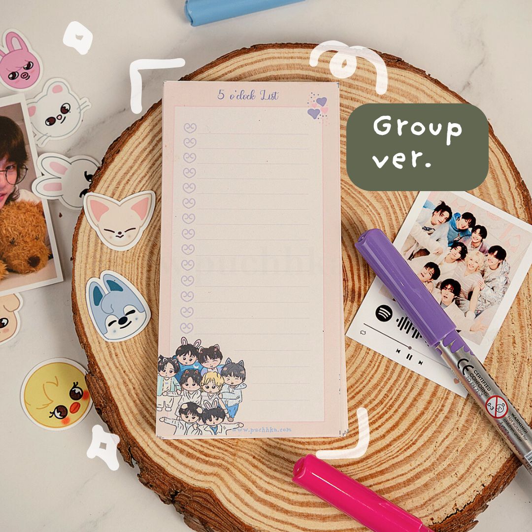 A pink notepad with a checklist and cartoon character illustration at the bottom, styled on a round wood slice with stickers, a purple marker, a pink marker, and group photo prints. A green label reads 'Group ver.