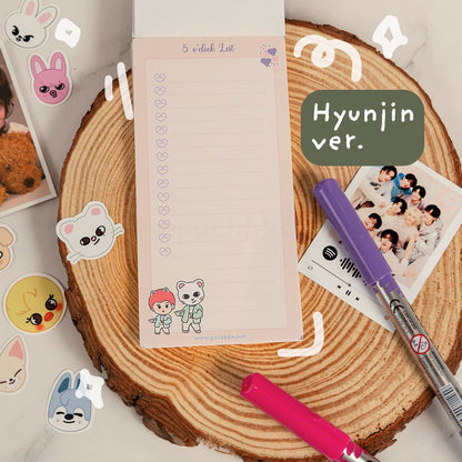 A styled flat-lay of a K-pop merchandise notepad featuring the text '5 o'clock List' and 'Hyunjin ver.' with cute cartoon character illustrations.