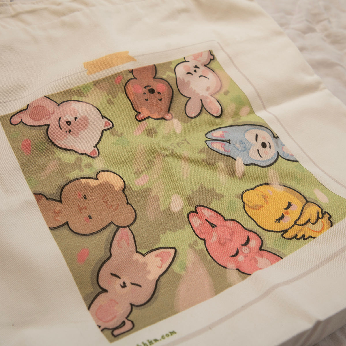 A close-up of a white fabric item, likely a pillowcase or cushion cover, featuring a printed square graphic of cute skzoo in pastel colors on a green background.