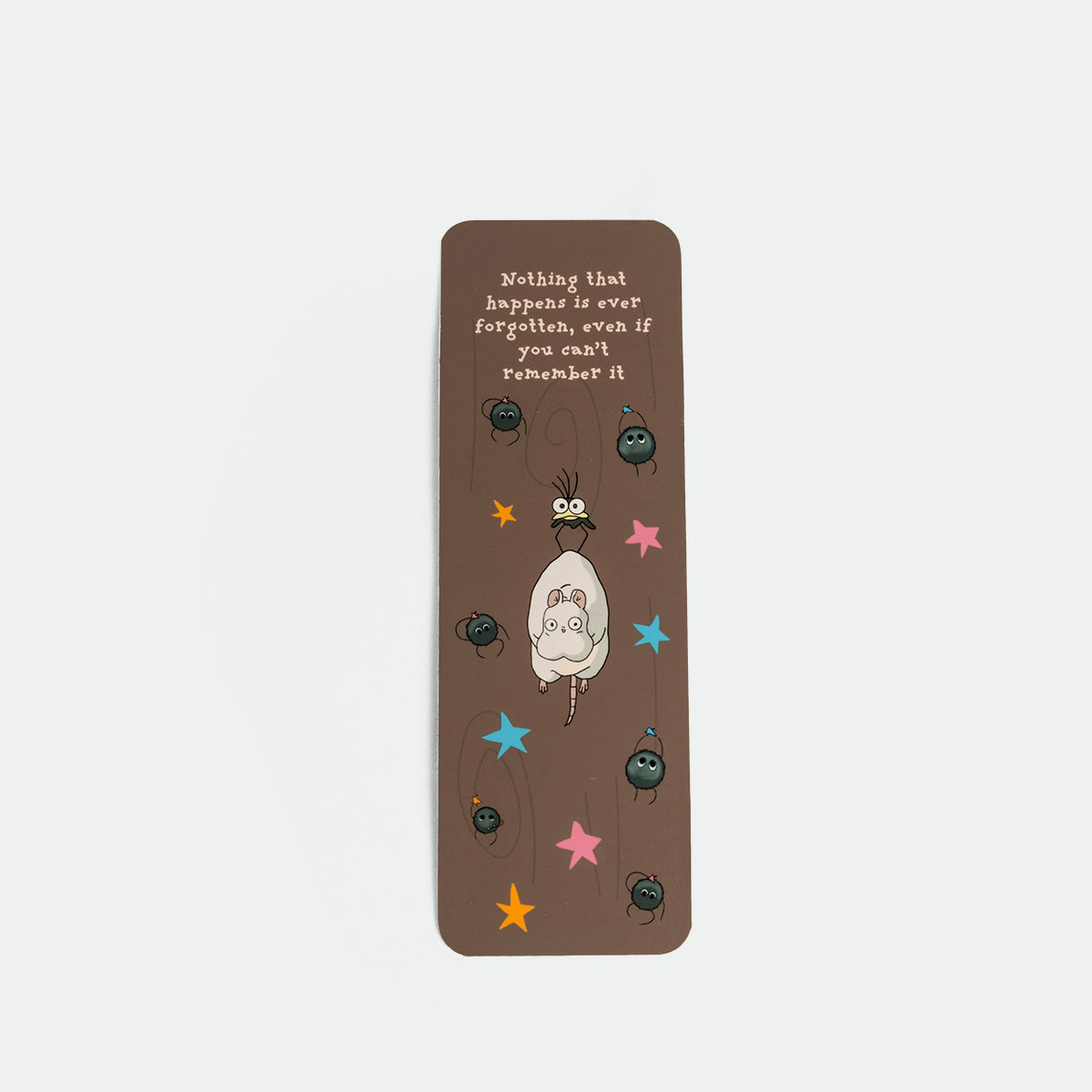 A brown rectangular bookmark featuring a ghibli illustration , colorful stars, and the quote 'Nothing that happens is ever forgotten, even if you can't remember it.'.