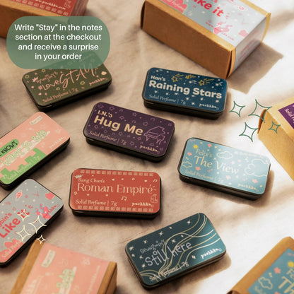 A styled flat-lay of multiple small rectangular perfume sample boxes with illustrated covers, arranged on a light surface with a kraft box and a green text bubble. The visible perfume names include LoveStay, Raining Stars, Hug Me, The View, Roman Empire, and Stay Here.