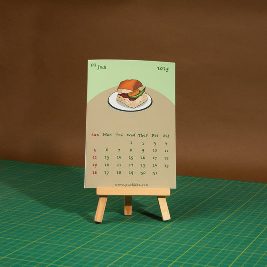 A novelty monthly calendar card featuring a hand-drawn hamburger illustration, displayed on a small wooden easel stand over a green cutting mat against a brown backdrop.