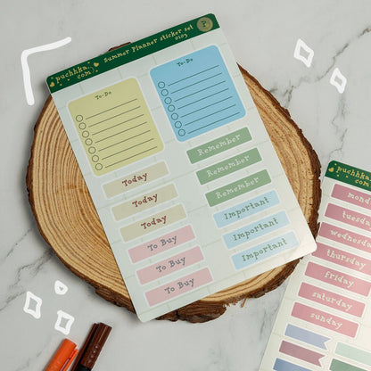 A sheet of pastel planner sticker labels from Puchhka.com is displayed on a round wood slice coaster over a light marble surface.