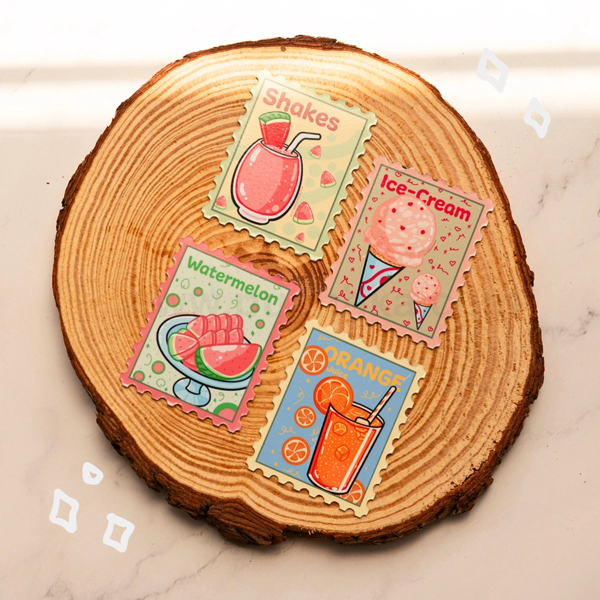 Four colorful illustrated dessert-themed stamp-like magnets are arranged on a round wood slice coaster over a light marble surface. The designs show a pink shake, a pink ice cream cone, a watermelon glass, and an orange shake, with labels reading Shakes, Ice-Cream, Watermelon, and Orange.