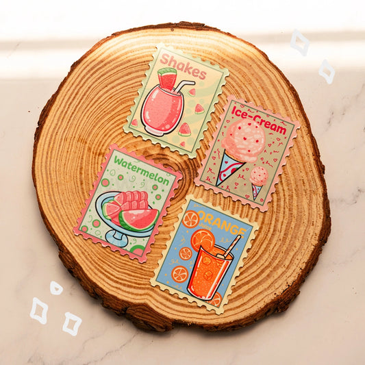 Four colorful illustrated dessert-themed stamp-like magnets are arranged on a round wood slice coaster over a light marble surface. The designs show a pink shake, a pink ice cream cone, a watermelon glass, and an orange shake, with labels reading Shakes, Ice-Cream, Watermelon, and Orange.