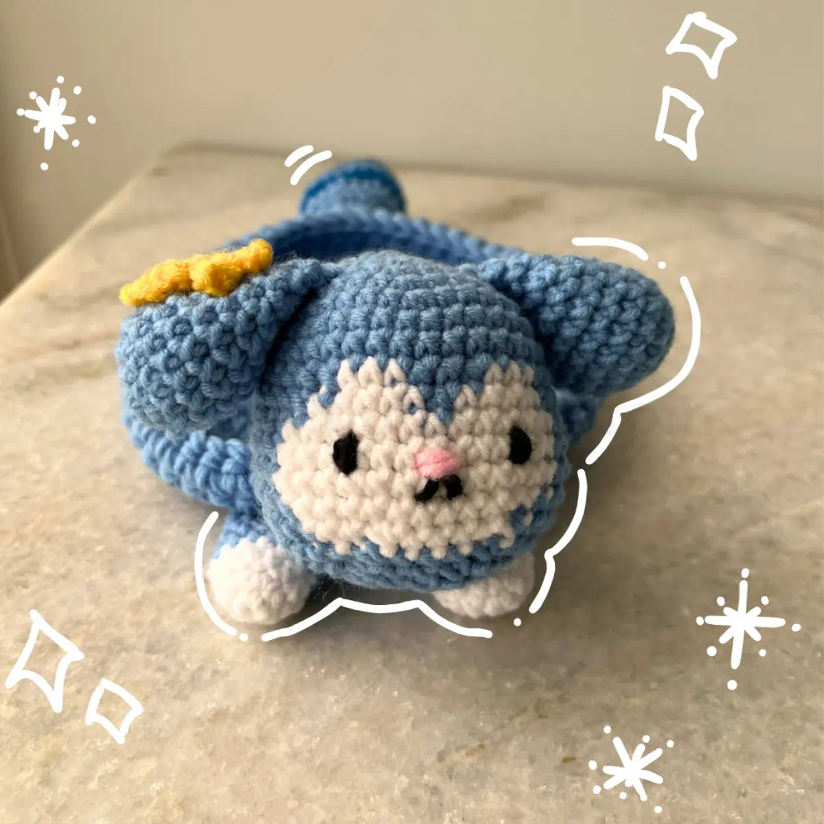 A handmade blue and white crochet Tasy tray with a small yellow bow, resting on a beige marble-like surface.