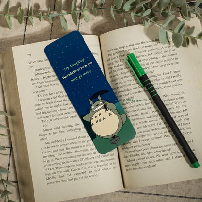 A small Totoro character bookmark , placed on an open book with a green pen resting on top.