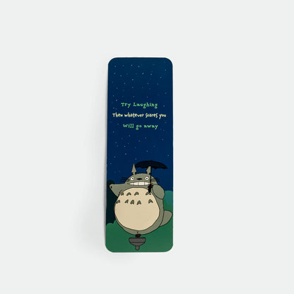 A slim rectangular bookmark of Totoro illustration from My Neighbor Totoro under a dark blue night sky with the quote 'Try Laughing. Then whatever scares you will go away' in green text.