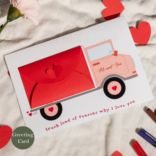 A Valentine's Day greeting card featuring a  red truck with the words 'Me and You' and 'truck load of reasons why I love you'. The card is displayed on a textured white fabric with red heart cutouts and a pink flower.