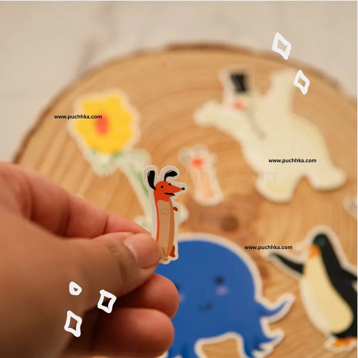 A hand holds a small die-cut sticker of weenie, with other characters stickers displayed on a round wooden slice in the blurred background.